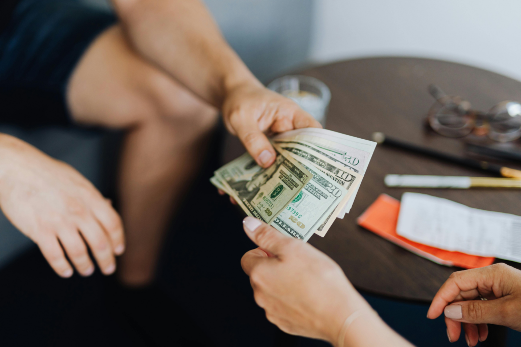 Tenant handing over dollar bills to another person with a blurred background showing a coffee table, coffee glass, receipt, and pens. This image represents Orlando security deposit deductions.