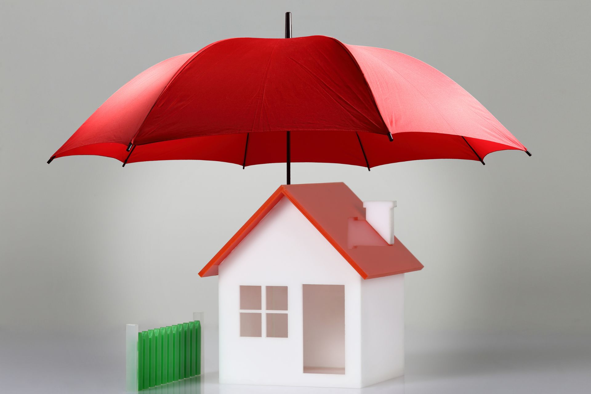 Red umbrella over a white house model to symbolize investment property protection