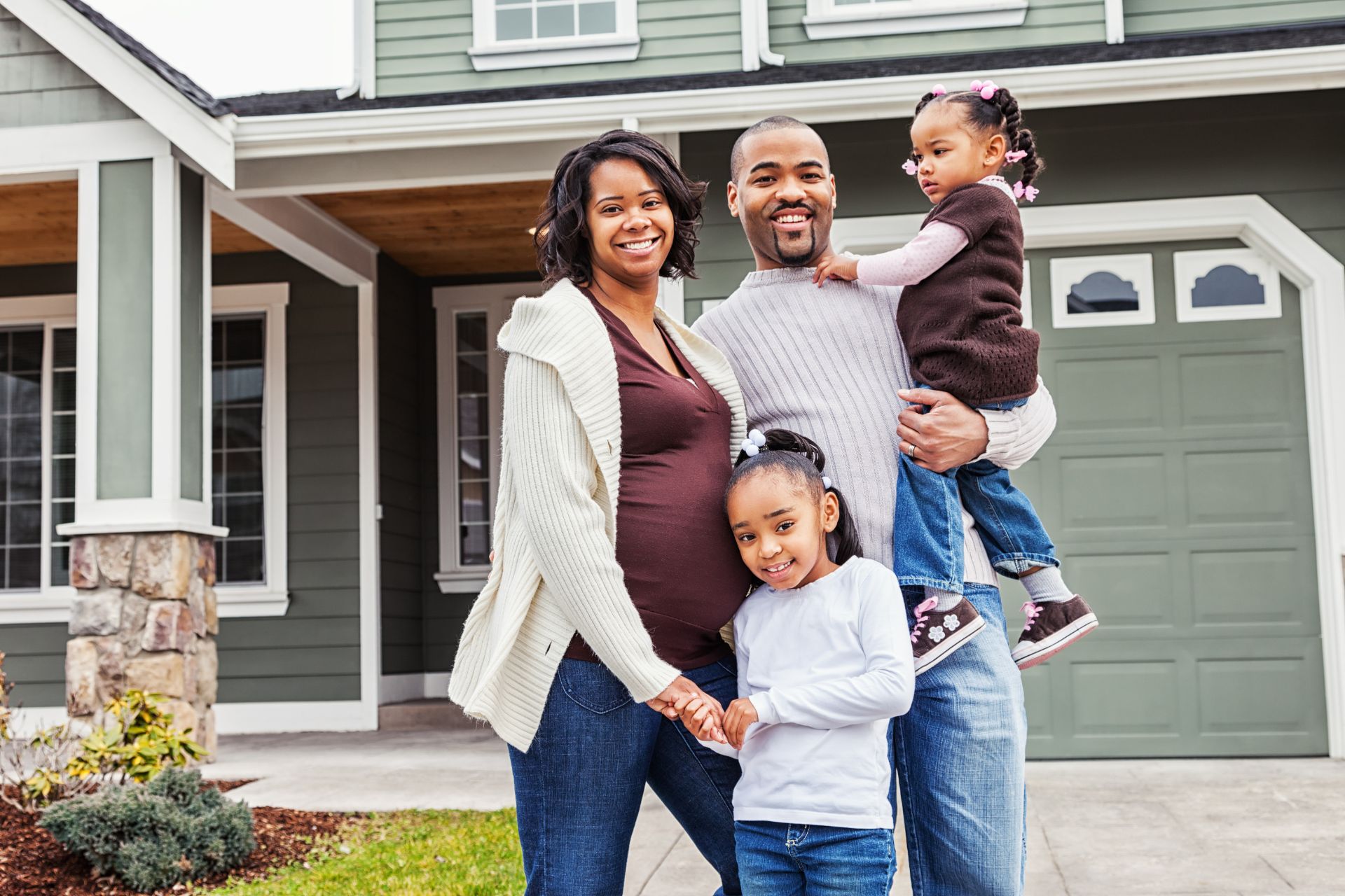 A family of four smiles in front of their well-maintained grey and white home, showcasing the inviting curb appeal that helps attract high-quality renters.