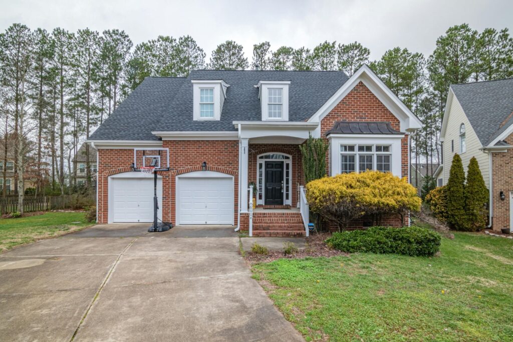 A white and brown brick house with a basketball hoop, a driveway and a grassy front yard with a bush, showcasing a well-maintained exterior typical of Orlando HOAs