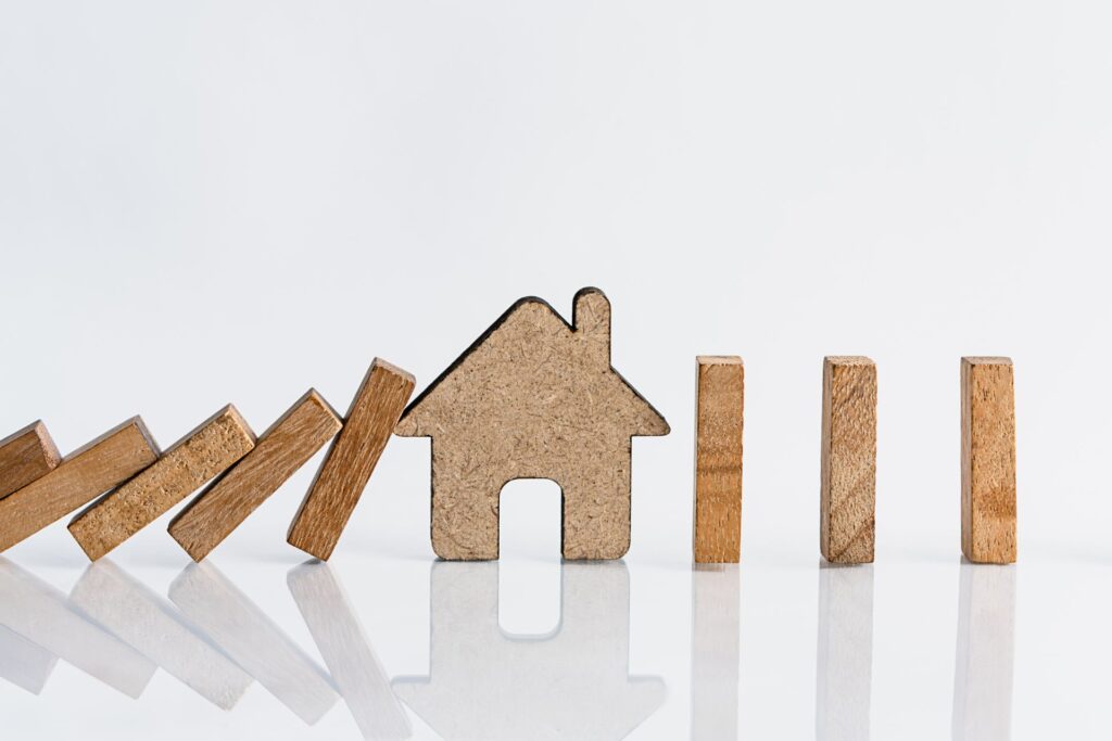 Miniature wooden blocks tumbling onto a small wooden house model against a white background, representing Orlando rental risk management.