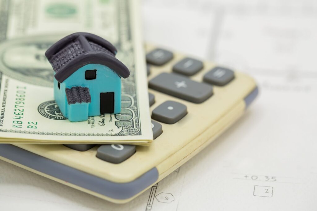 A miniature house balancing on dollar bills and a calculator, representing the world of financing real estate investments.