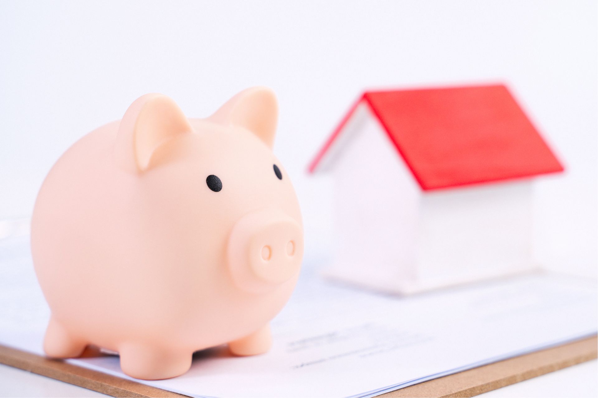 A light pink piggy bank on a clipboard with paperwork highlights budgeting tips for Central Florida renters, while a blurred model house in the background symbolizes homeownership.