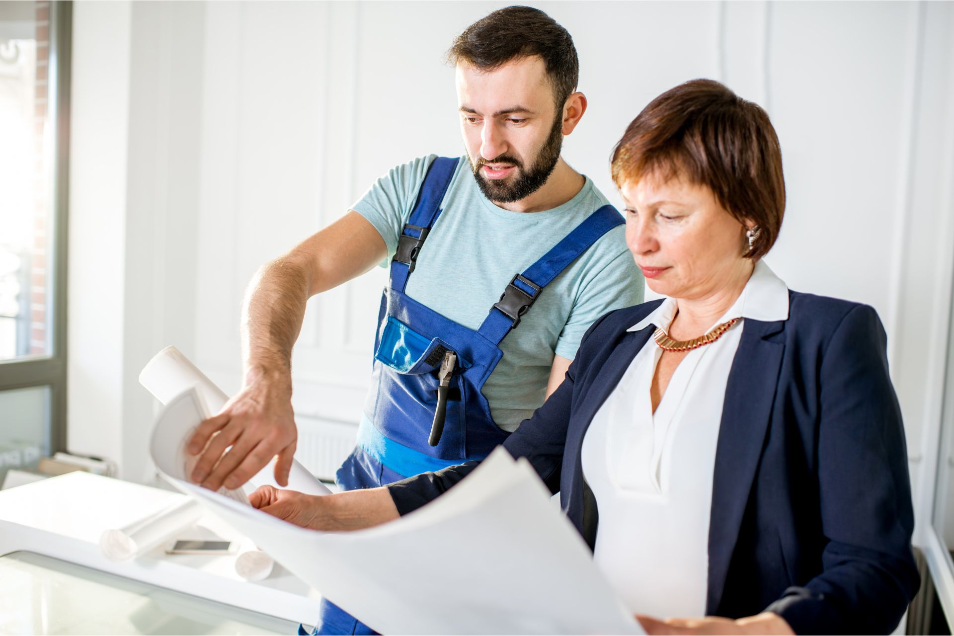 A trusted male repair vendor in overalls works with a female property owner in a suit, reviewing plans on paper for Orlando rental repairs.