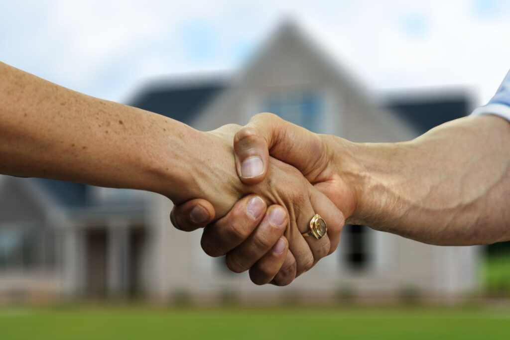 Shaking hands in front of a blurred house, symbolizing a deal being finalized. Hiring a property manager in Orlando could be the key to securing a successful investment.